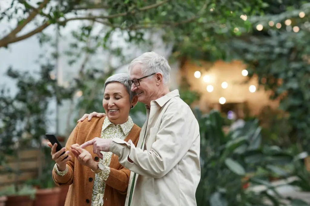 Elderly couple smiling together as they view something on a cell phone