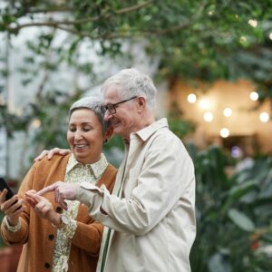 Elderly couple smiling together as they view something on a cell phone
